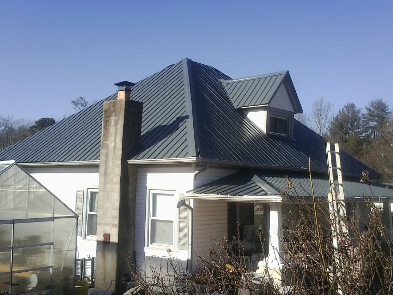 Dark blue standing seam metal roof on a white farmhouse with dormer — Slate & Tile Roof Repair by Roofing Brothers in Armington