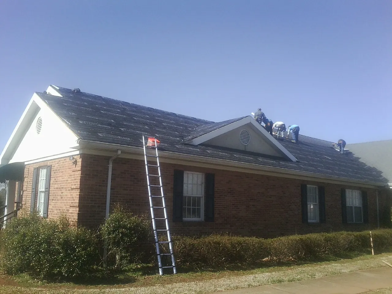 Crew tearing shingles off a brick ranch roof with a ladder set — Emergency Roof Repair work by our crew in Armington