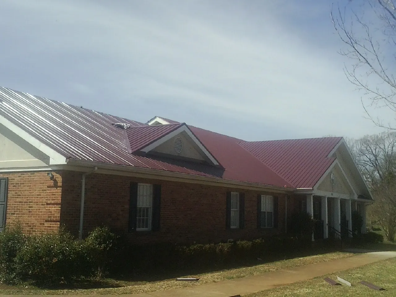 Red metal roof with gabled entries on a long brick building, from a Hail Damage Roof Repair job in Armington
