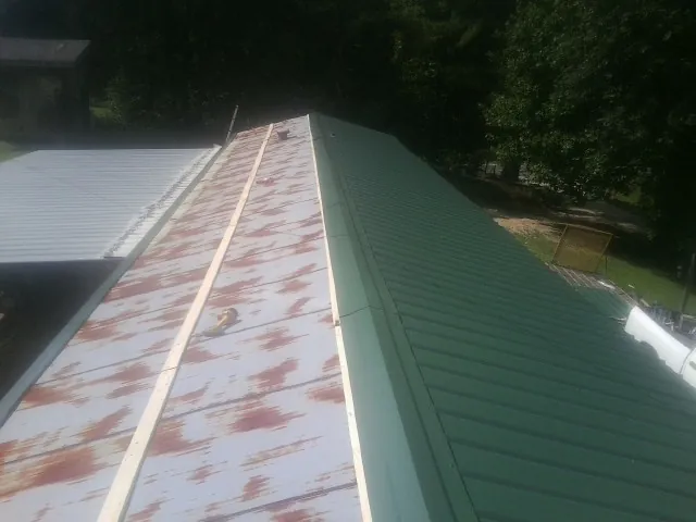 Old rusted panels beside newly installed green metal roofing — Wind Damage Roof Repair by Roofing Brothers in Armington