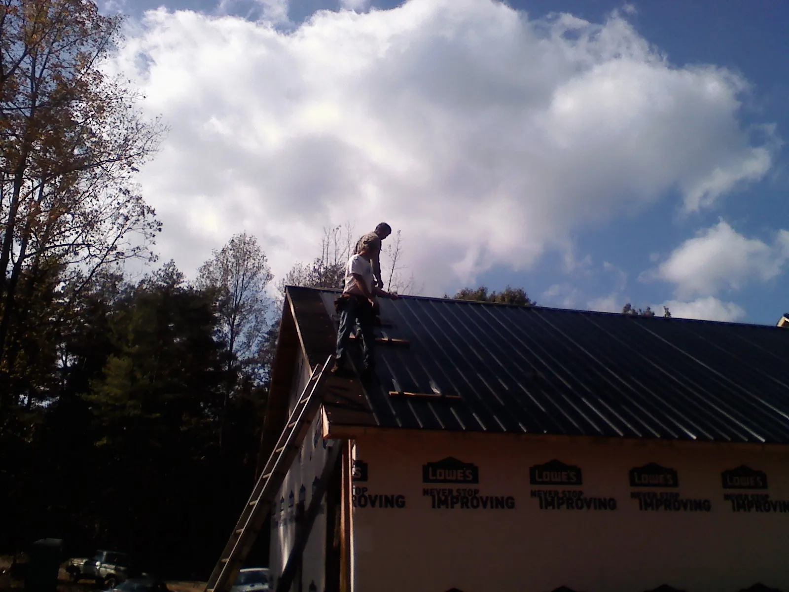 Roofer fastening dark metal panels high against a cloudy sky, from a Roof Inspection job in Armington
