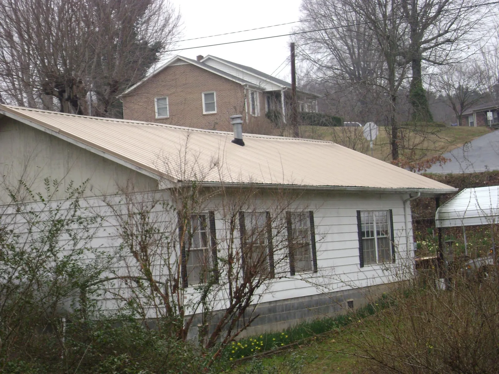 Tan metal roof on a white sided house set into a hillside — Commercial Roofing by Roofing Brothers in Armington